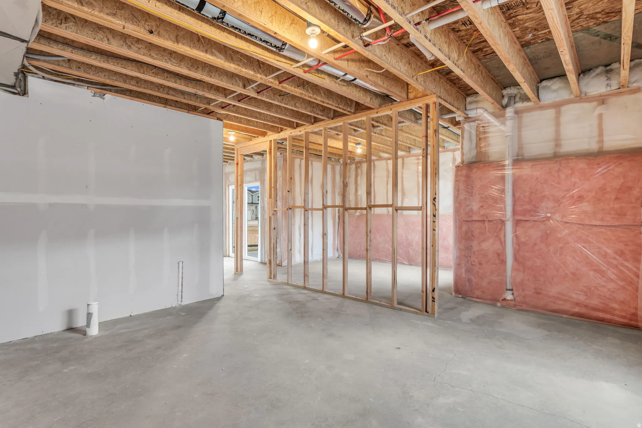 Unfinished interior space with exposed ceiling joists, framed wall structures, installed insulation, and a concrete floor