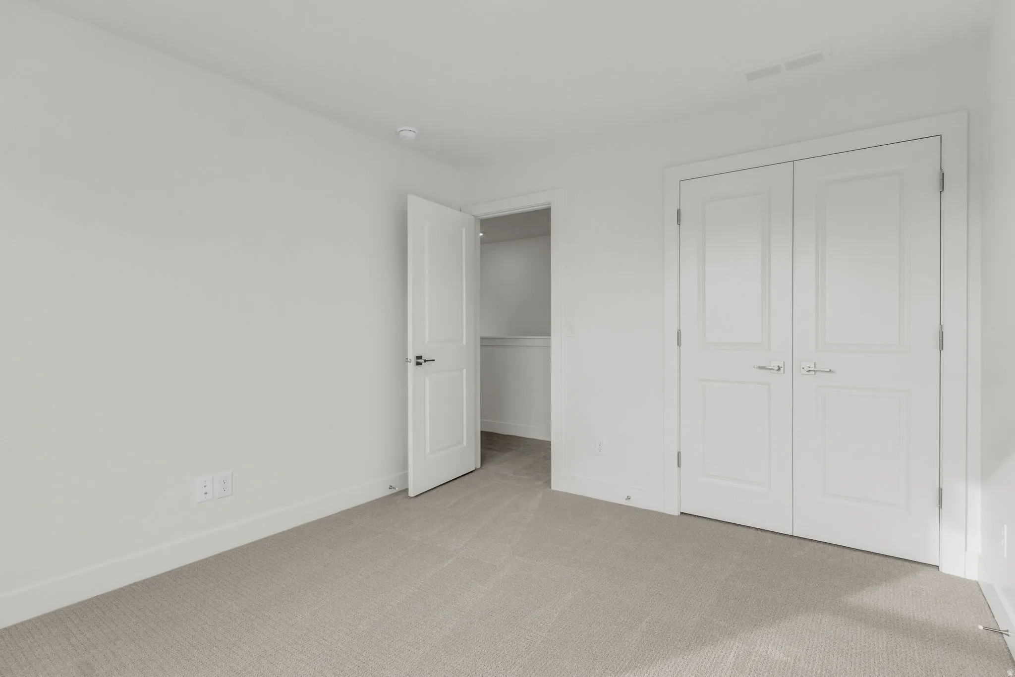 Neutral-toned carpeting, white walls, and a white paneled door with black hardware