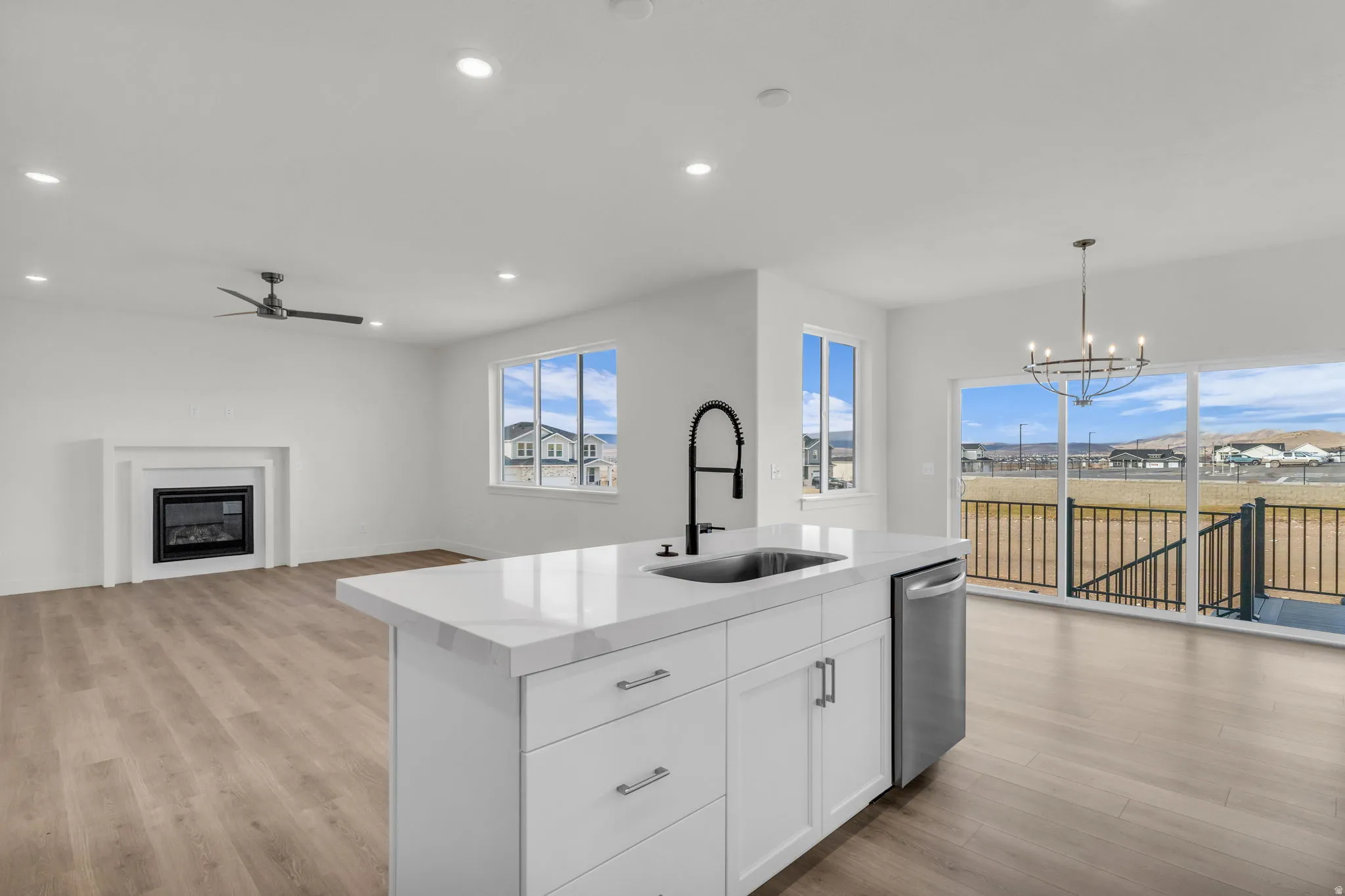 Open-concept kitchen and living area featuring a large white island with waterfall-edge countertop, stainless steel appliances, and a professional pull-down faucet