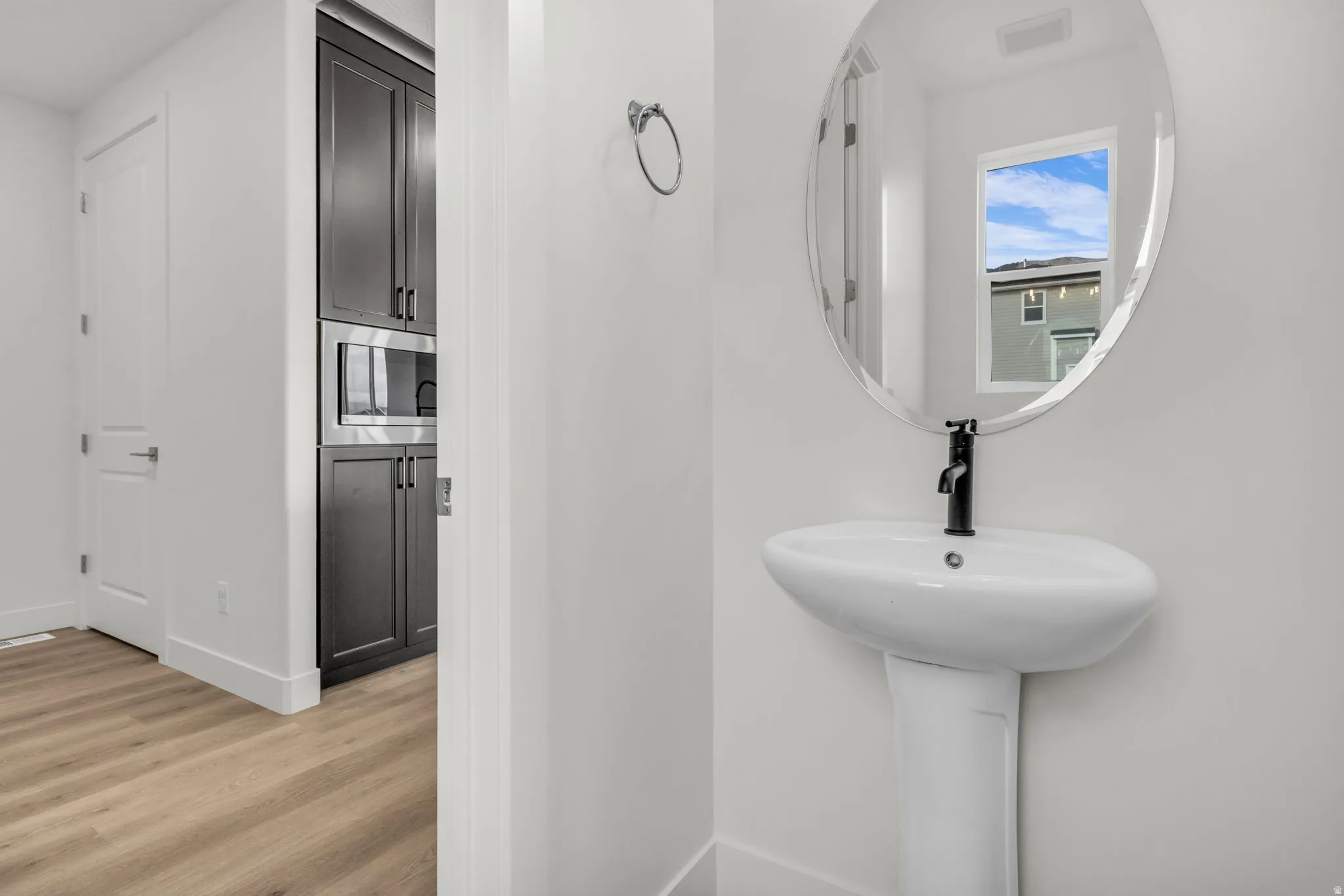 Modern bathroom featuring a pedestal sink with matte black faucet, oval wall-mounted mirror, and wood-finish flooring throughout