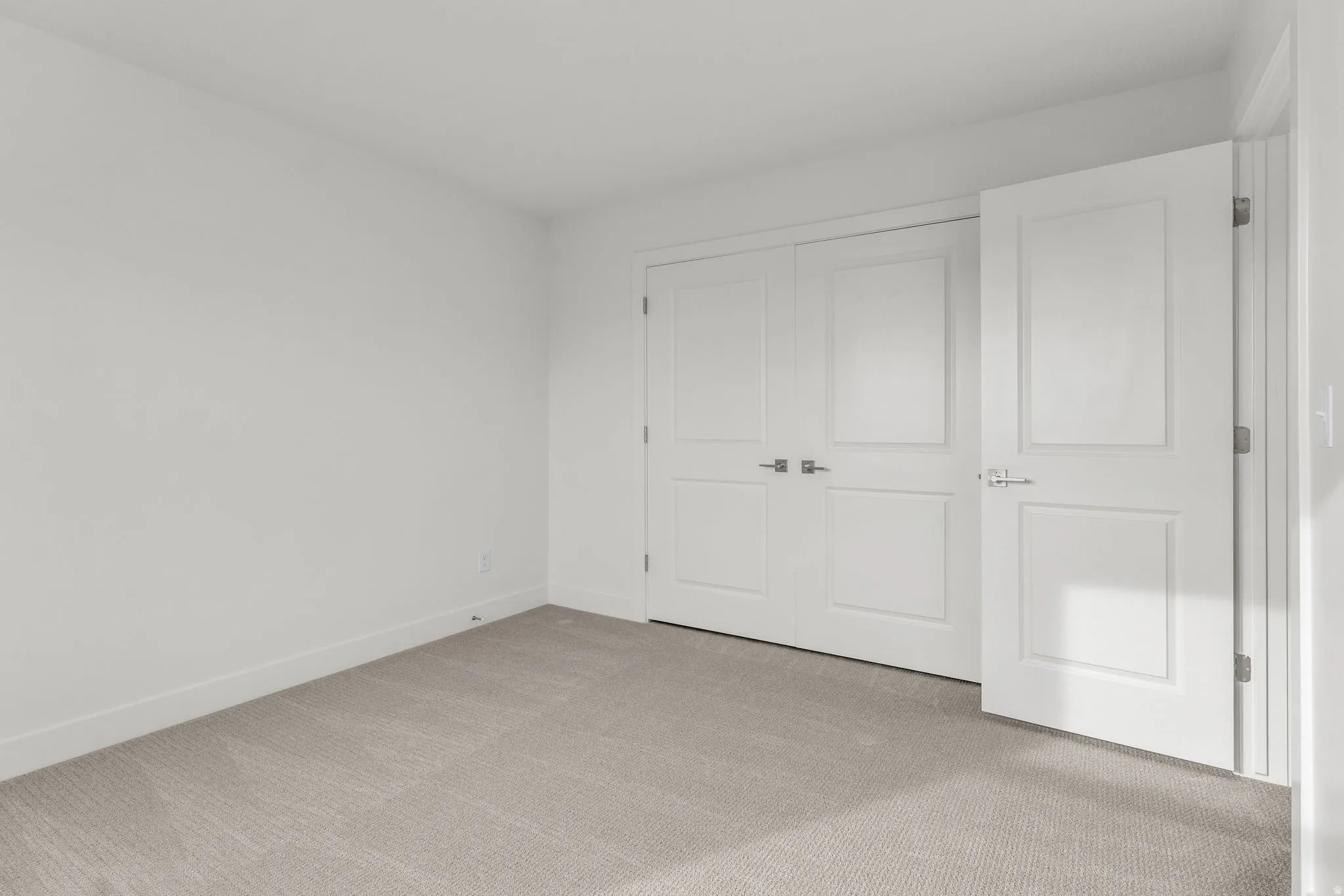 Bright, light-filled bedroom featuring pristine white panel doors with polished hardware, neutral wall finishes, and soft gray carpet flooring throughout