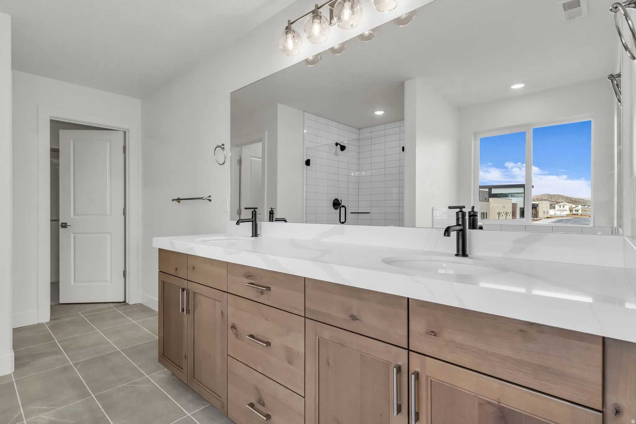 Spa-inspired primary bathroom featuring an expansive dual-sink vanity with wood-finish cabinetry, white quartz countertops, and matte black hardware