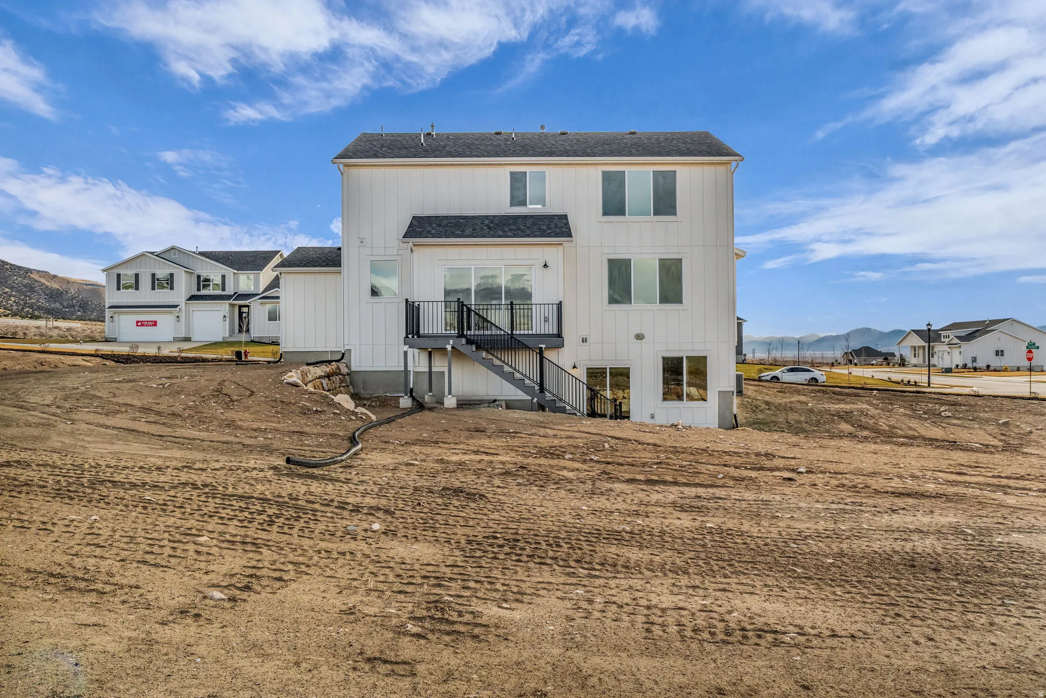 Modern farmhouse-style residence featuring a clean white exterior with multiple levels, black-trimmed windows, and a covered entry deck with metal railings