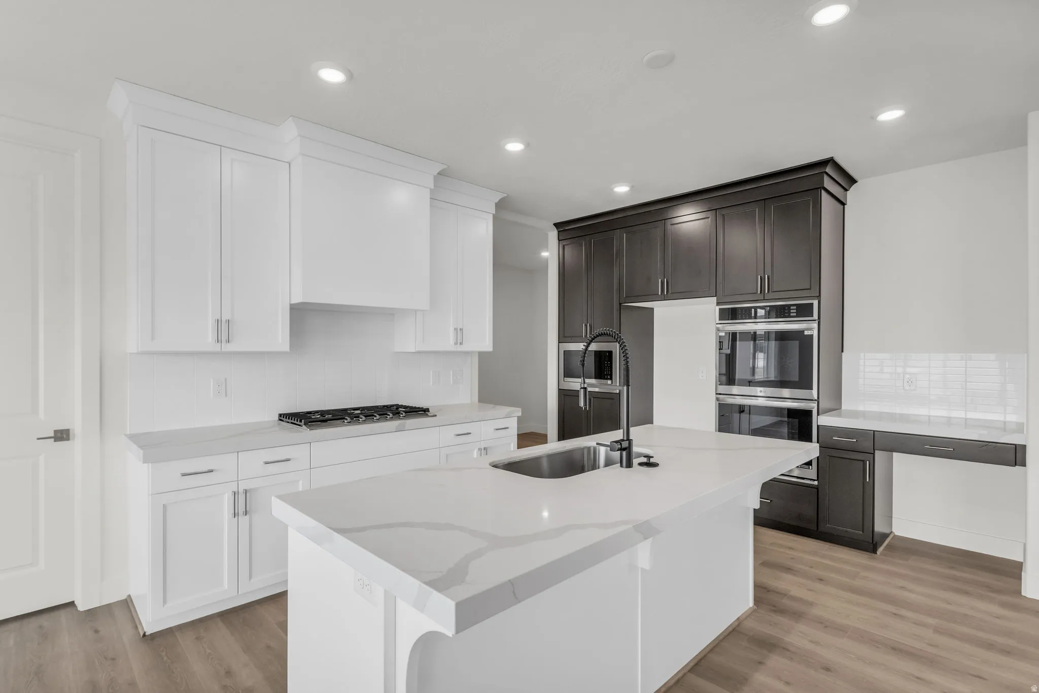 Kitchen featuring a large island with an integrated sink, white cabinetry, dark wood-finish cabinetry, and stainless steel built-in appliances