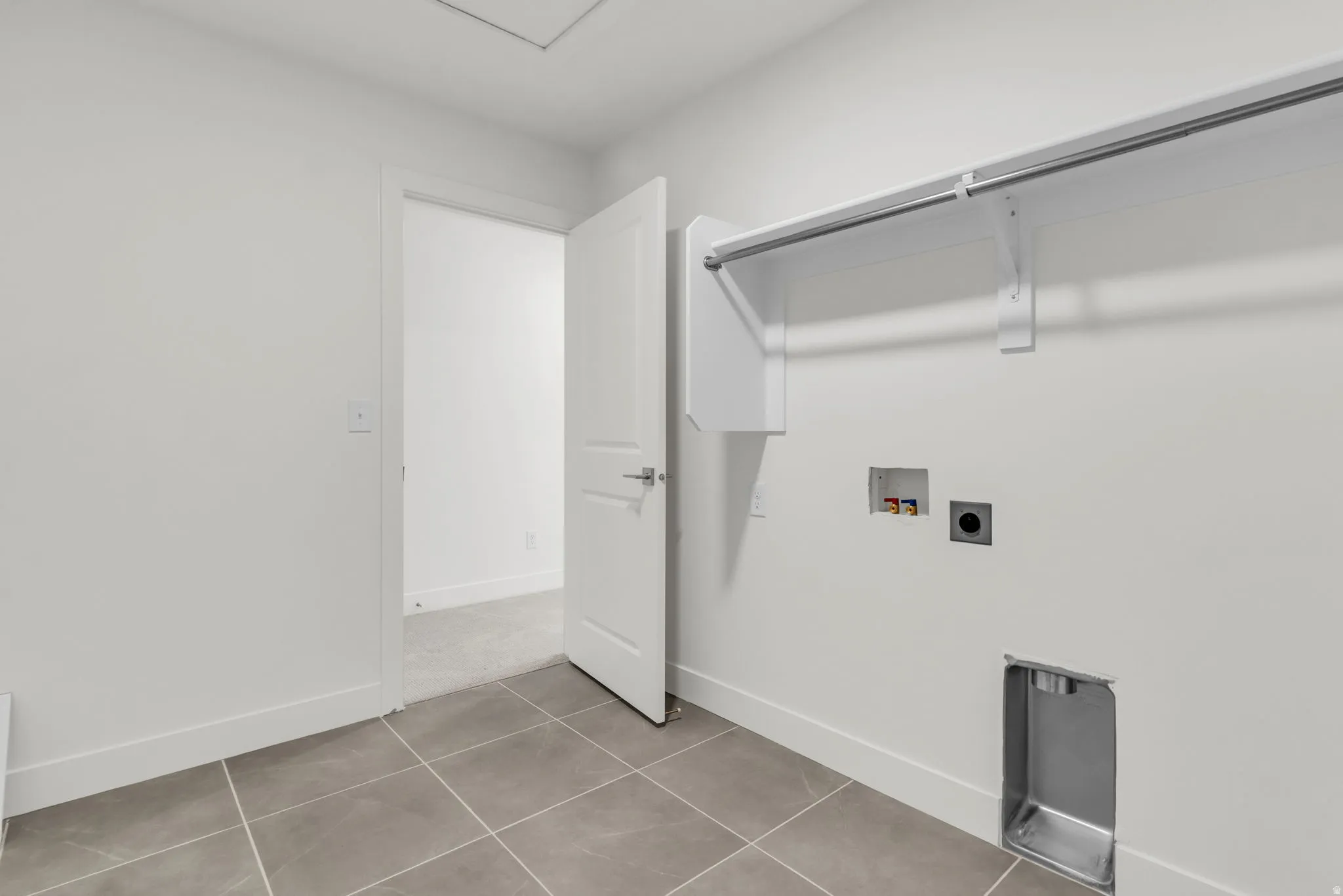 Modern laundry room featuring tile flooring, a chrome rod with sliding shower curtain, stainless steel appliance cutouts, and dual electrical outlets with cover plates