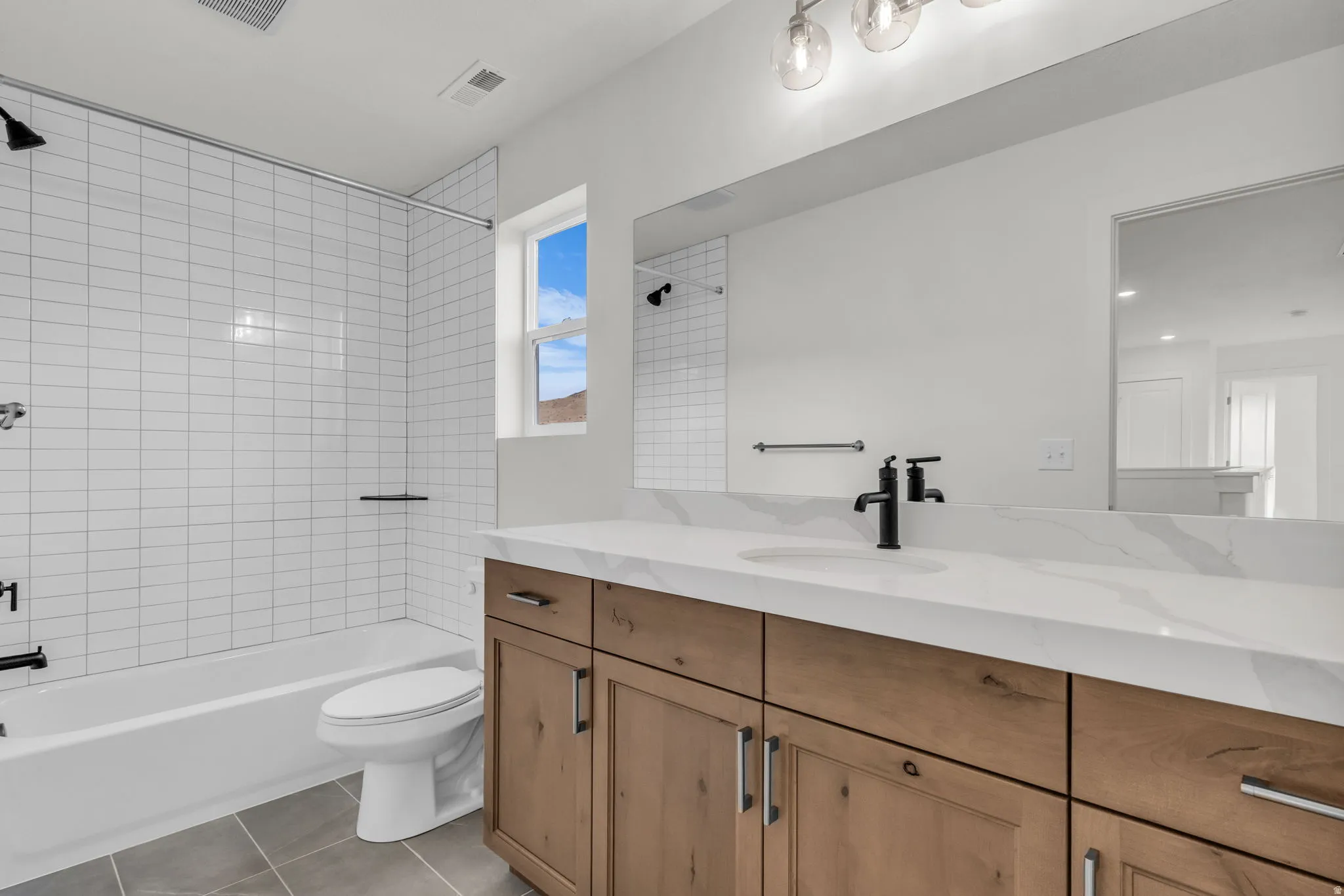 Spa-inspired secondary bathroom featuring a wood stained cabinetry with ample storage, white quartz countertop, and matte black fixtures and hardware.