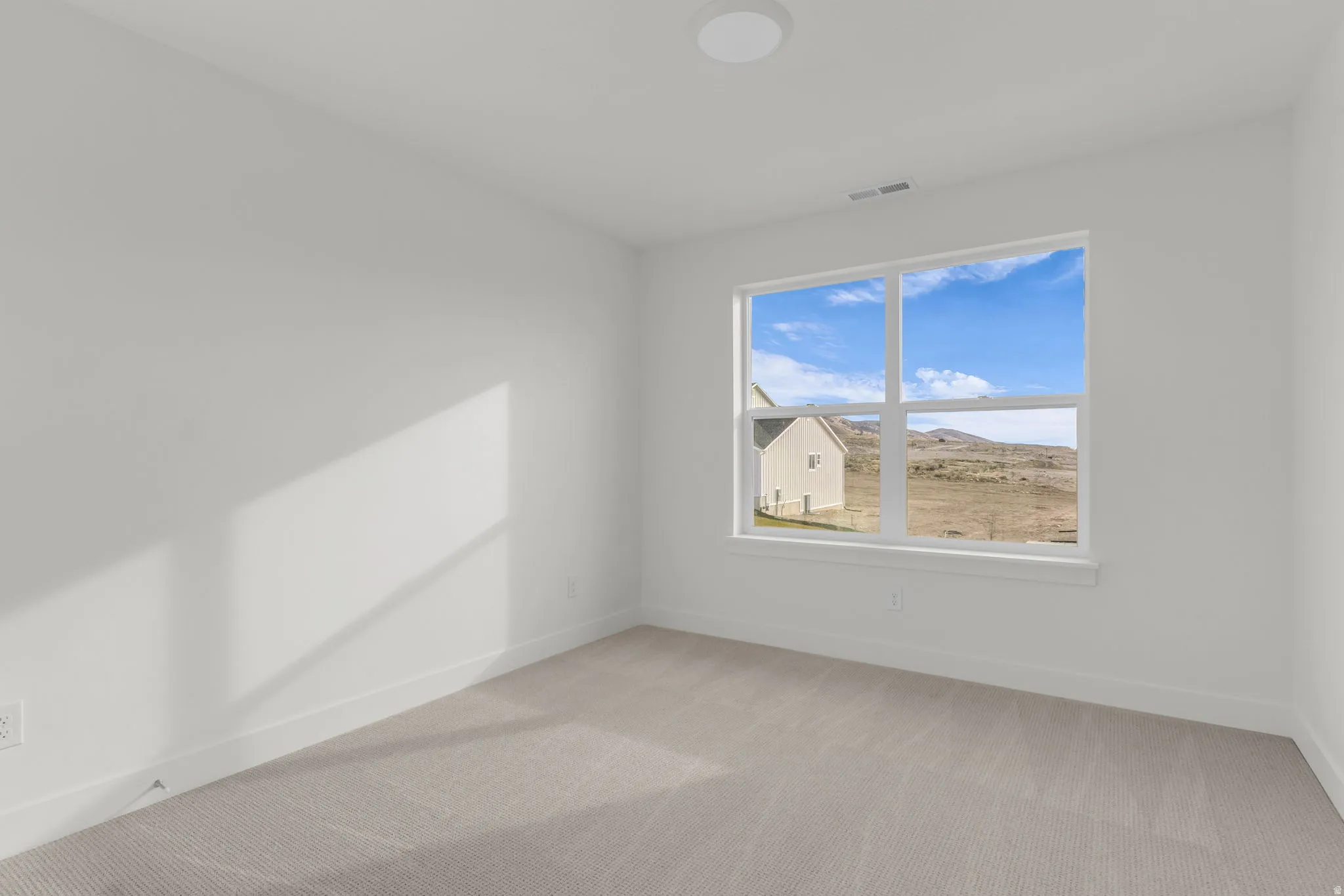 Bright, naturally lit bedroom featuring large double-hung windows framing expansive landscape vistas, neutral wall finishes, and plush carpeting throughout