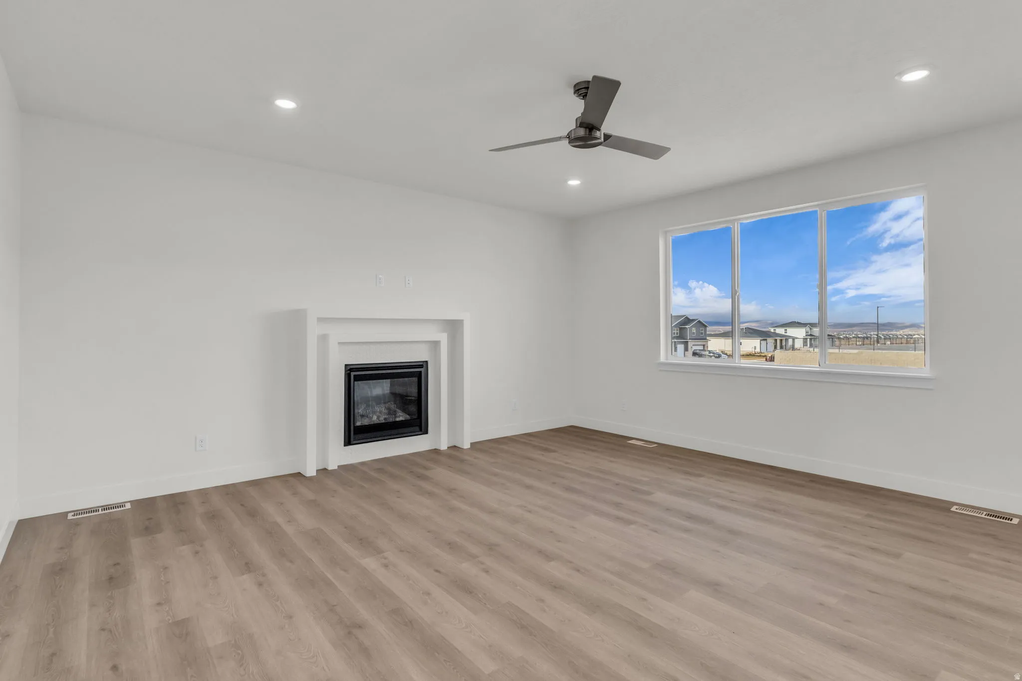 Spacious room with wood-finish flooring, a contemporary ceiling fan, and recessed lighting