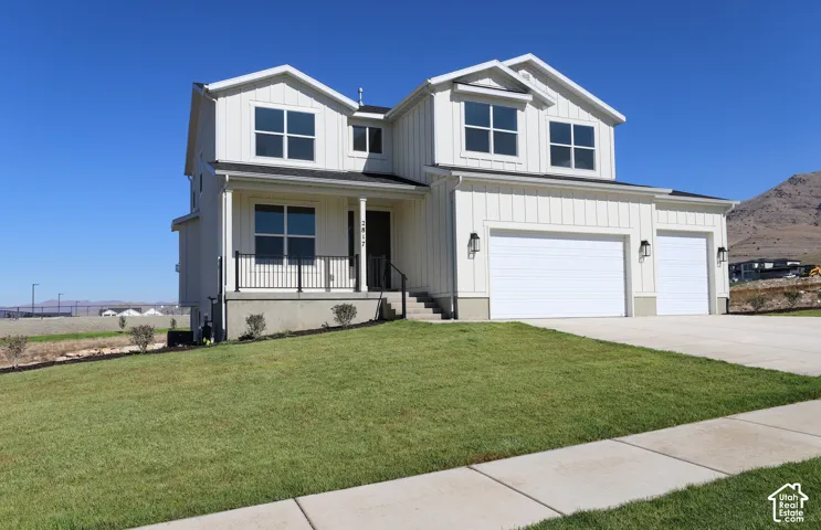 Contemporary farmhouse exterior with white vertical siding, a covered front porch with black railing, a two-car garage, and a concrete driveway