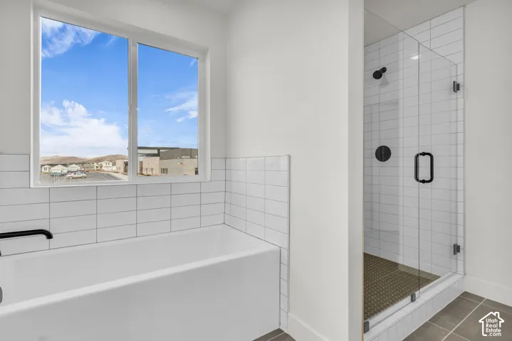 Modern primary bathroom featuring a freestanding soaking tub with subway tile surround, frameless glass walk-in shower enclosure with multiple showerheads and dark tile flooring, white subway tile walls, and a large window with expansive natural light and