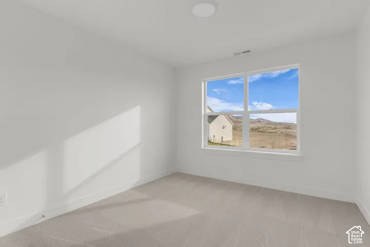 Bright, naturally lit bedroom featuring large double-hung windows framing expansive landscape vistas, neutral wall finishes, and plush carpeting throughout