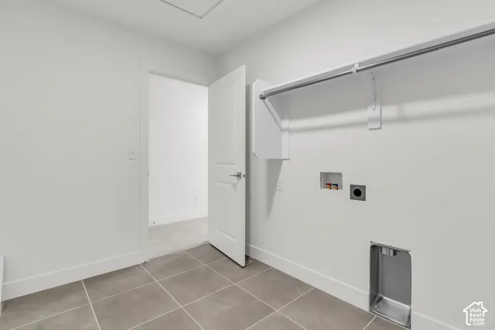 Modern laundry room featuring tile flooring, a chrome rod with sliding shower curtain, stainless steel appliance cutouts, and dual electrical outlets with cover plates