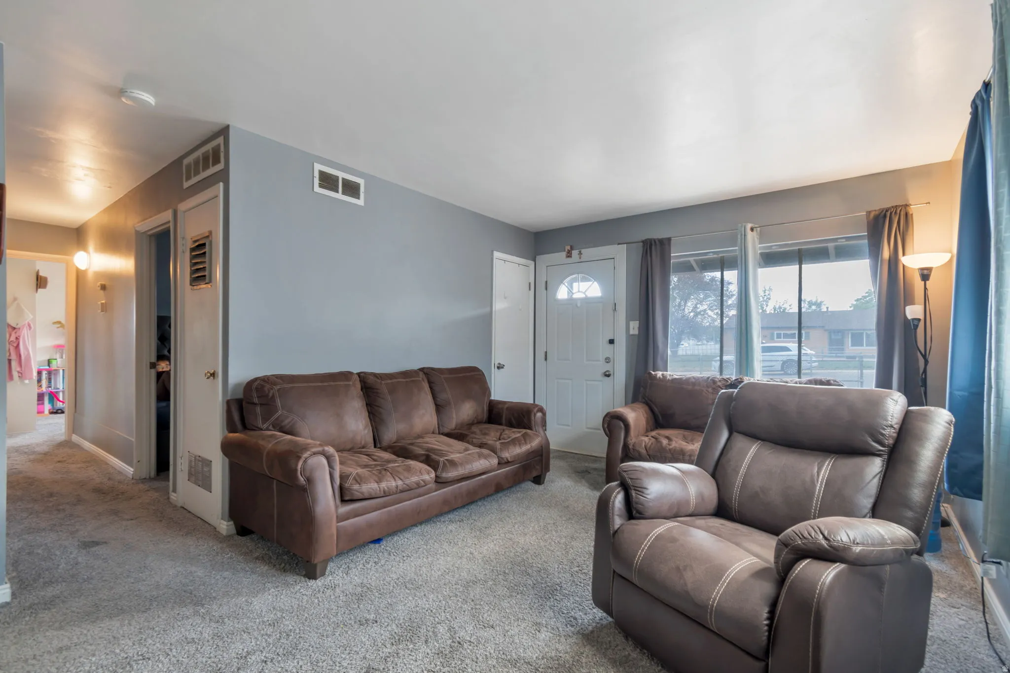Carpeted flooring, light gray wall paint, white trim, and a white front door with a decorative window