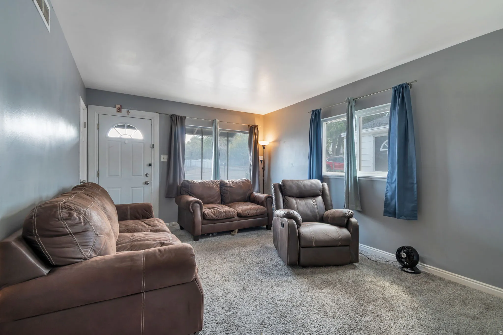Living area featuring a light gray carpet, multiple windows, and a front entry door with an arched transom window