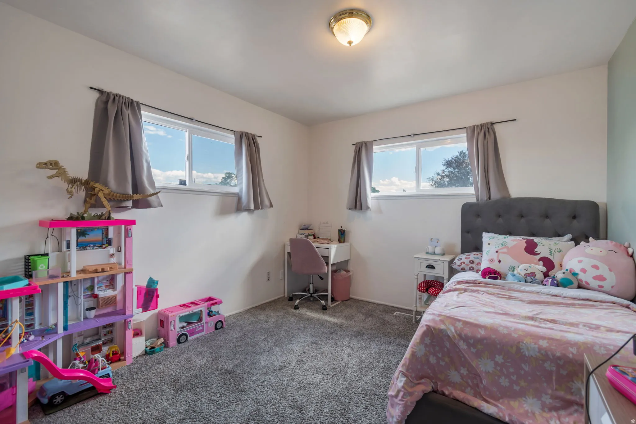 Plush grey carpeting, two large windows, overhead flush-mount lighting, and light-colored walls