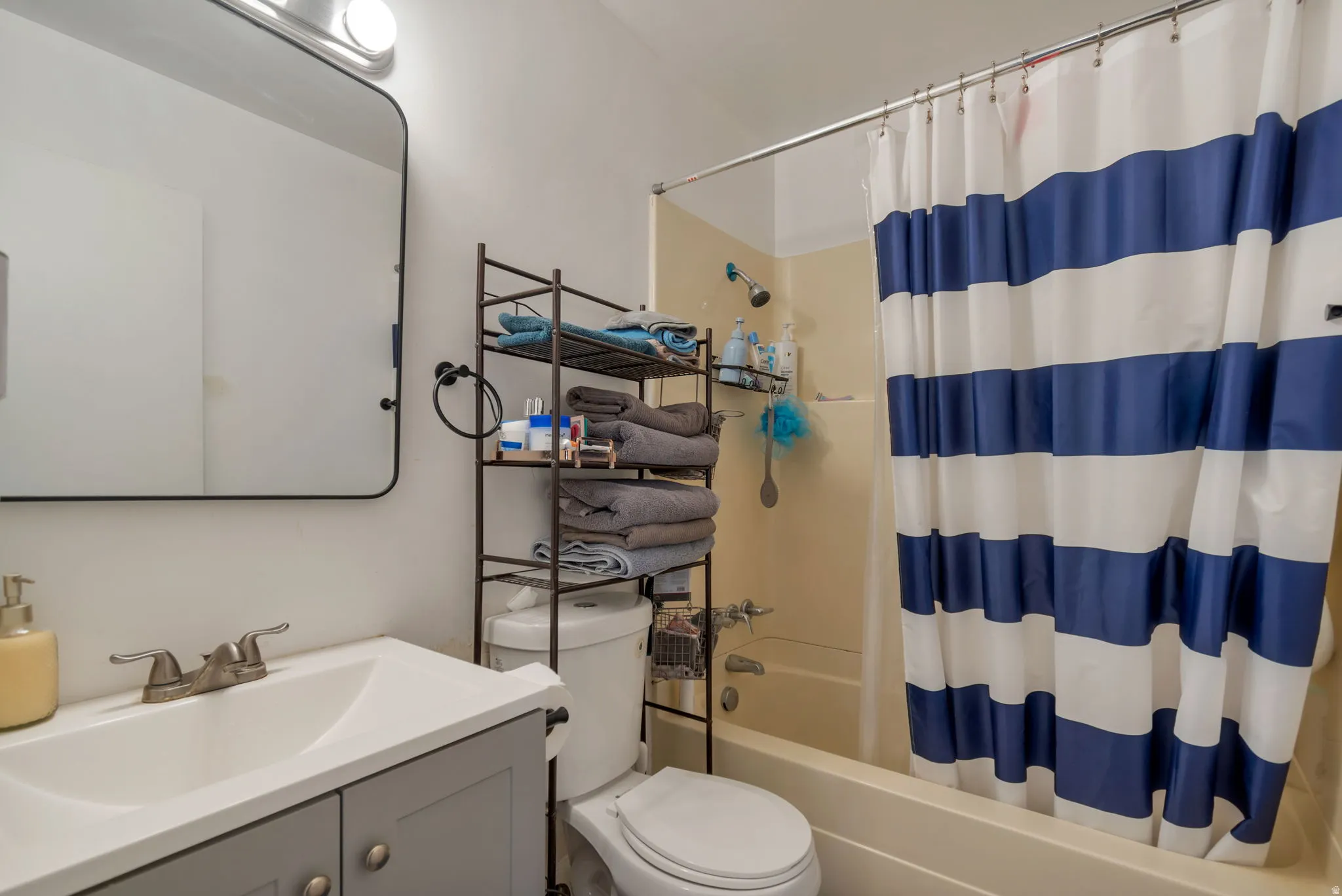 Vanity with an integrated sink and brushed nickel faucet, a rounded rectangular mirror, and a built-in shower/tub combination