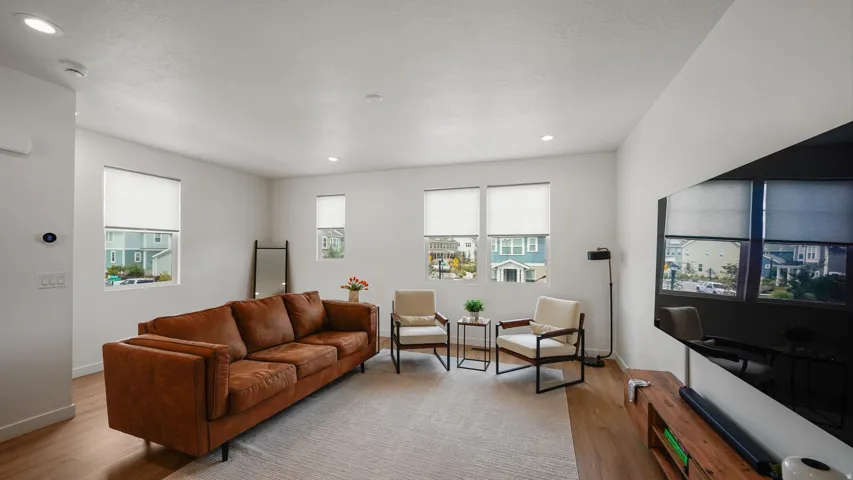 Wood-finish flooring, multiple windows with roller shades, recessed lighting, and a wall-mounted display