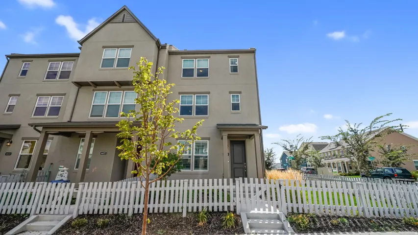 Three-story exterior with a stucco finish, multiple windows, a covered entrance, and a white picket fence