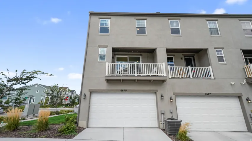 Multi-story townhouse with a stucco exterior, two private balconies with white railings, and an integrated garage