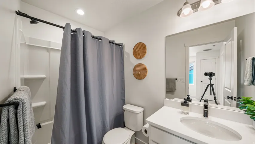 White vanity with integrated sink and chrome faucet, mounted mirror, shower/tub combination with white surround, and recessed ceiling lighting
