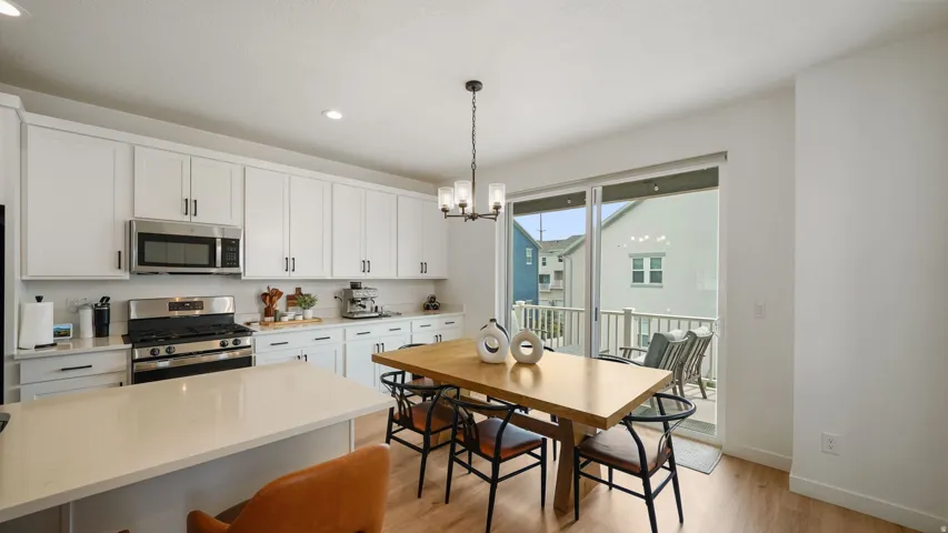 Kitchen featuring white shaker cabinetry, stainless steel appliances, light-toned countertops, wood-finish flooring, and direct access to an outdoor deck