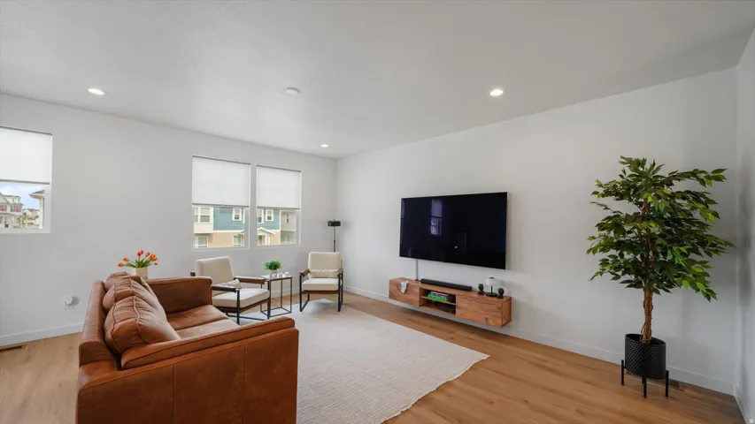 Recessed lighting, wood-finish flooring, multiple windows with roller shades, and a wall-mounted media console