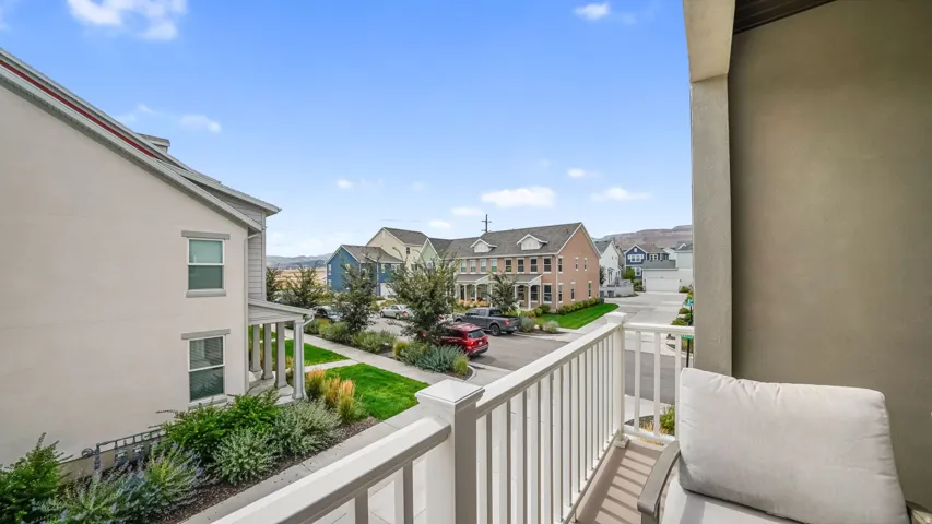 Private balcony with white railing overlooking a street and residential homes