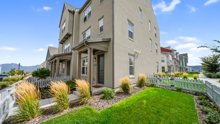 Stucco exterior with multiple windows, covered front porch, a picket fence, and a manicured lawn
