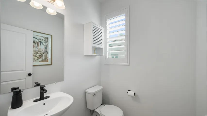 Wall-mounted sink with a black-finish faucet, built-in wall cabinet, and a window with white louvered shutters