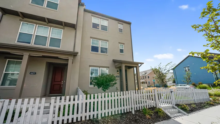 Three-story townhouse exterior with a white picket fence, covered entry, and multiple windows