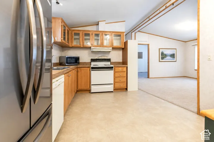 Stainless steel refrigerator, wood-finish cabinetry with glass accents, white appliances, and vinyl flooring