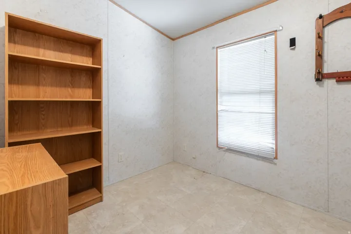 Built-in shelving unit, neutral wall paneling, window with blinds, and tile flooring