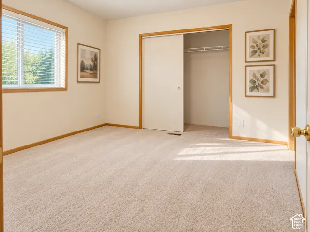 Primary Suite. Light beige wall paint, carpeted flooring, wood trim, window with blinds, and a closet with sliding doors