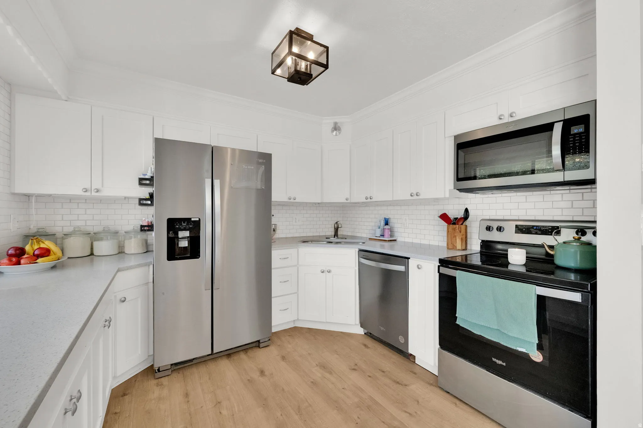 White cabinetry with brushed nickel hardware, stainless steel appliances, light-toned wood-finish flooring, white subway tile backsplash, and light-colored countertops