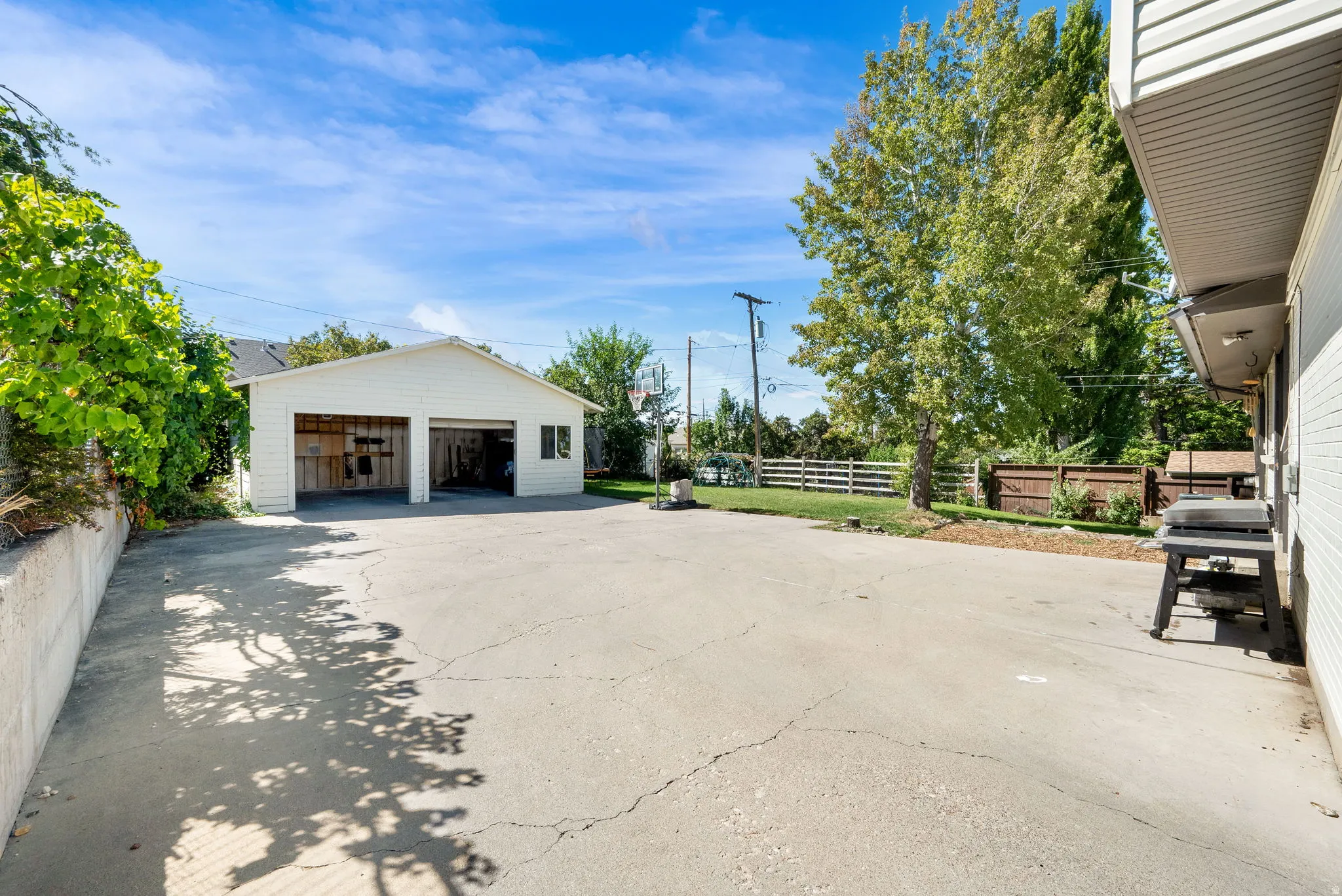 Detached two-car garage with white siding, expansive paved surface, and mature trees