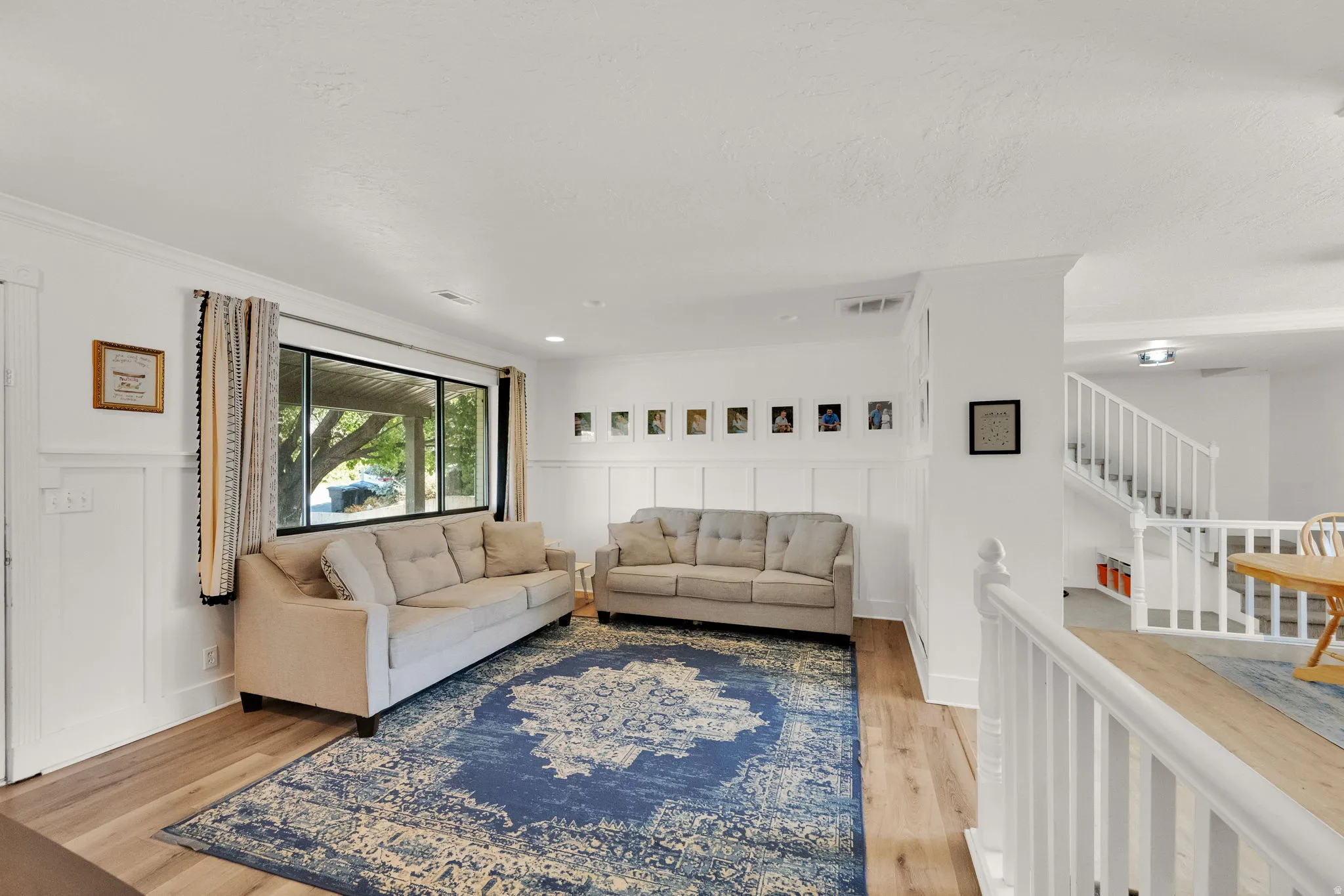 Open-concept living area featuring wood-finish flooring, white board and batten wall detailing, and a large window
