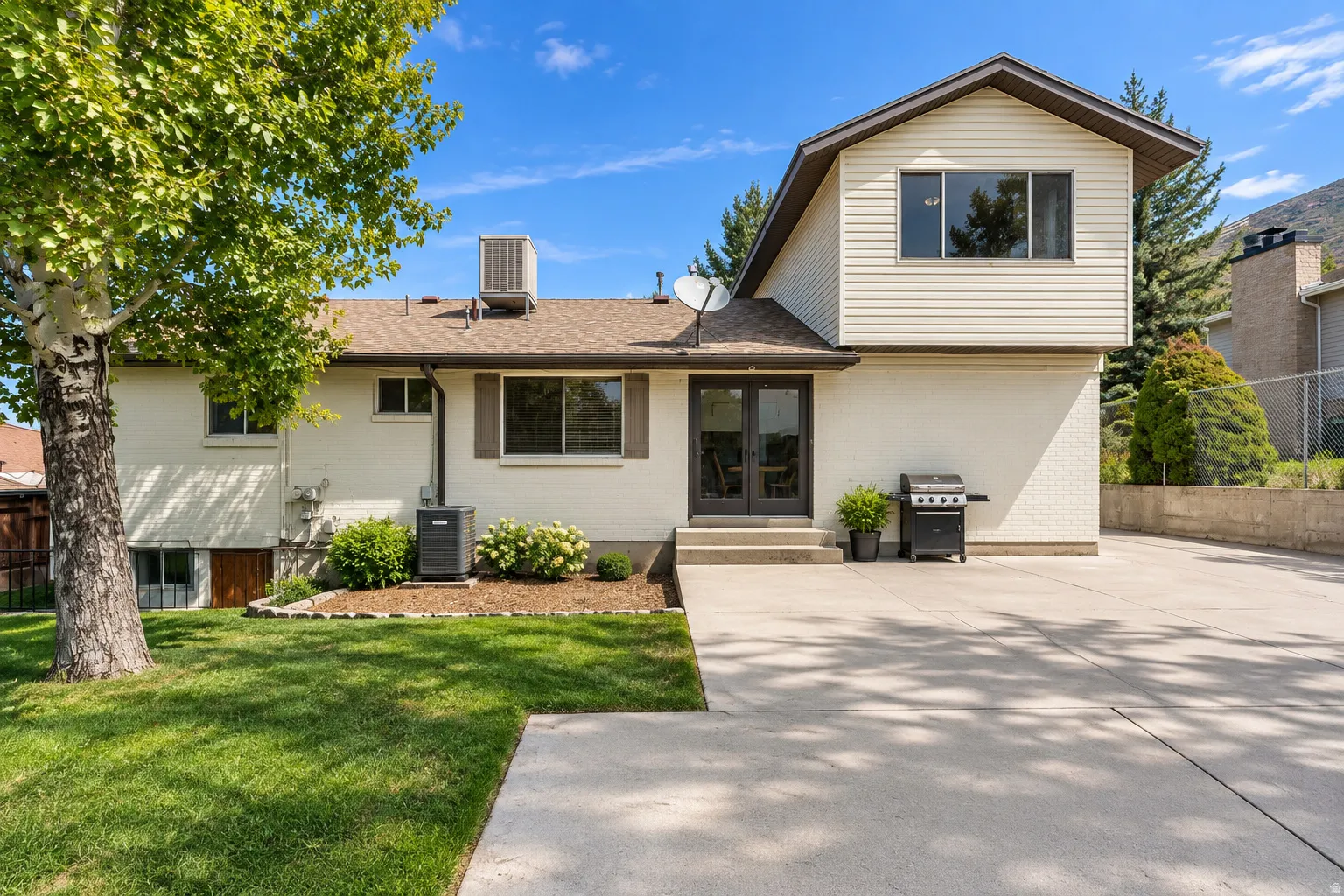 Exterior featuring a white brick and beige siding facade, multiple windows, double glass doors, and a concrete patio