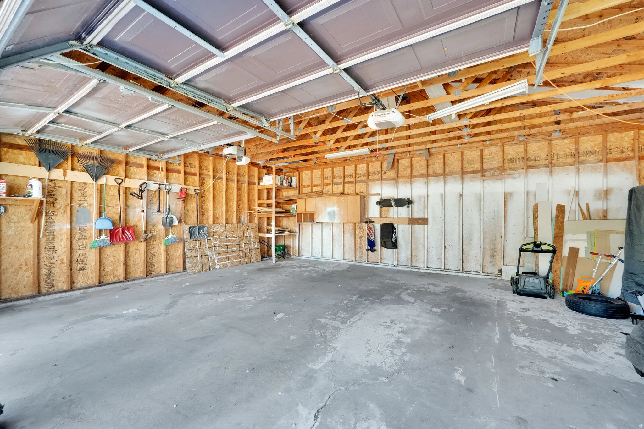 Attached garage with exposed wood framing, concrete flooring, overhead lighting, and built-in shelving