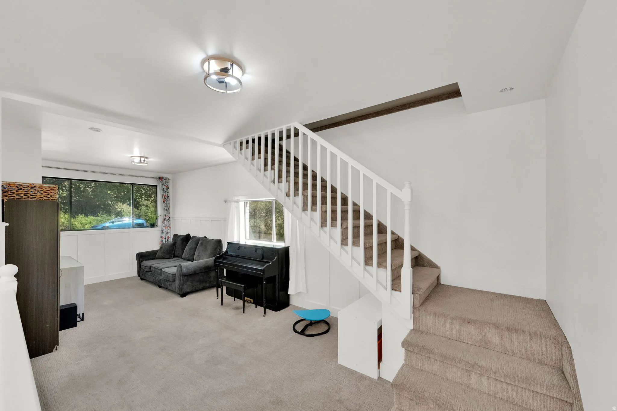 Carpeted living space with a multi-pane window, flush-mount ceiling lighting, and a carpeted staircase with white balusters