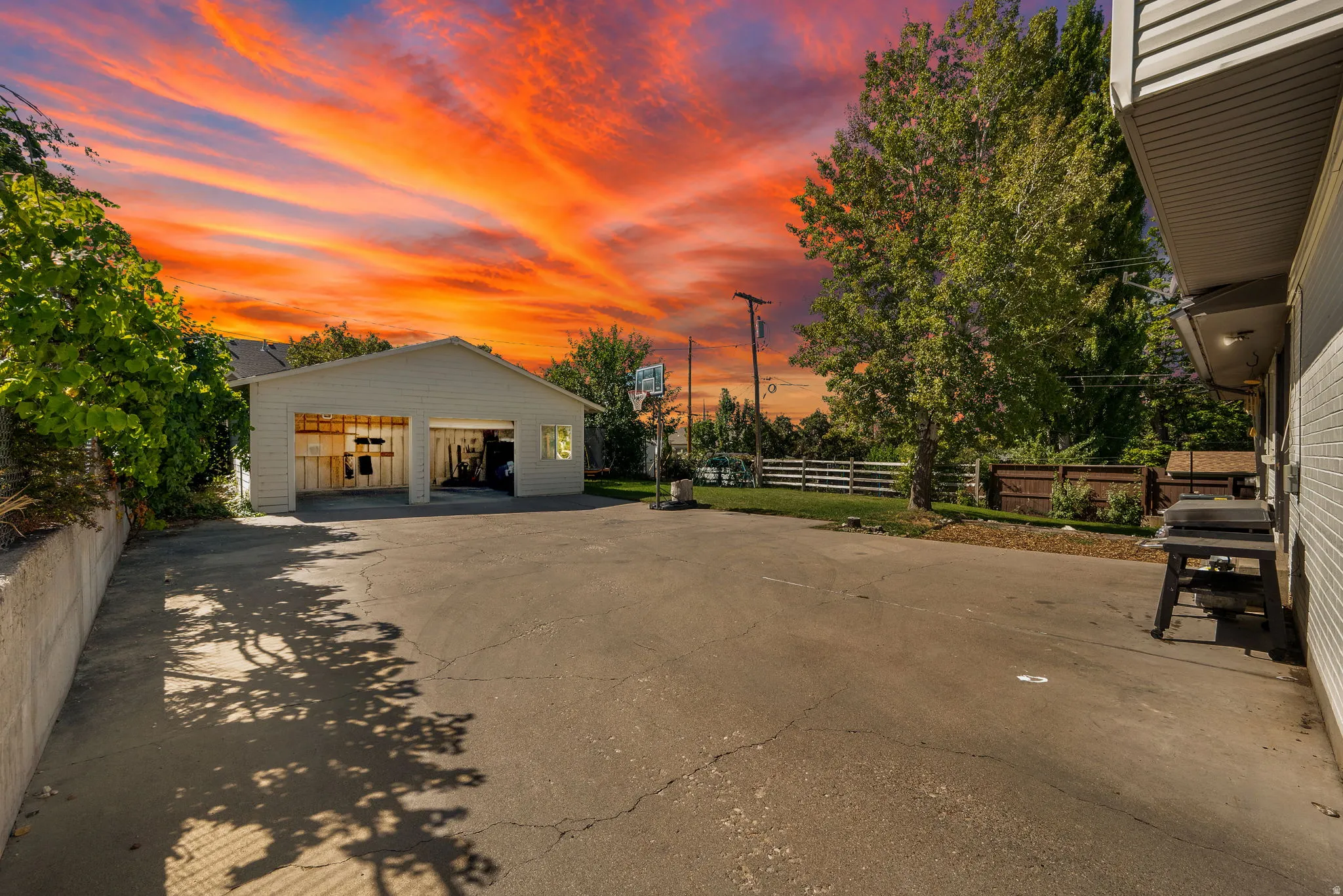 Detached two-car garage with overhead doors, paved driveway, concrete retaining wall, and mature trees