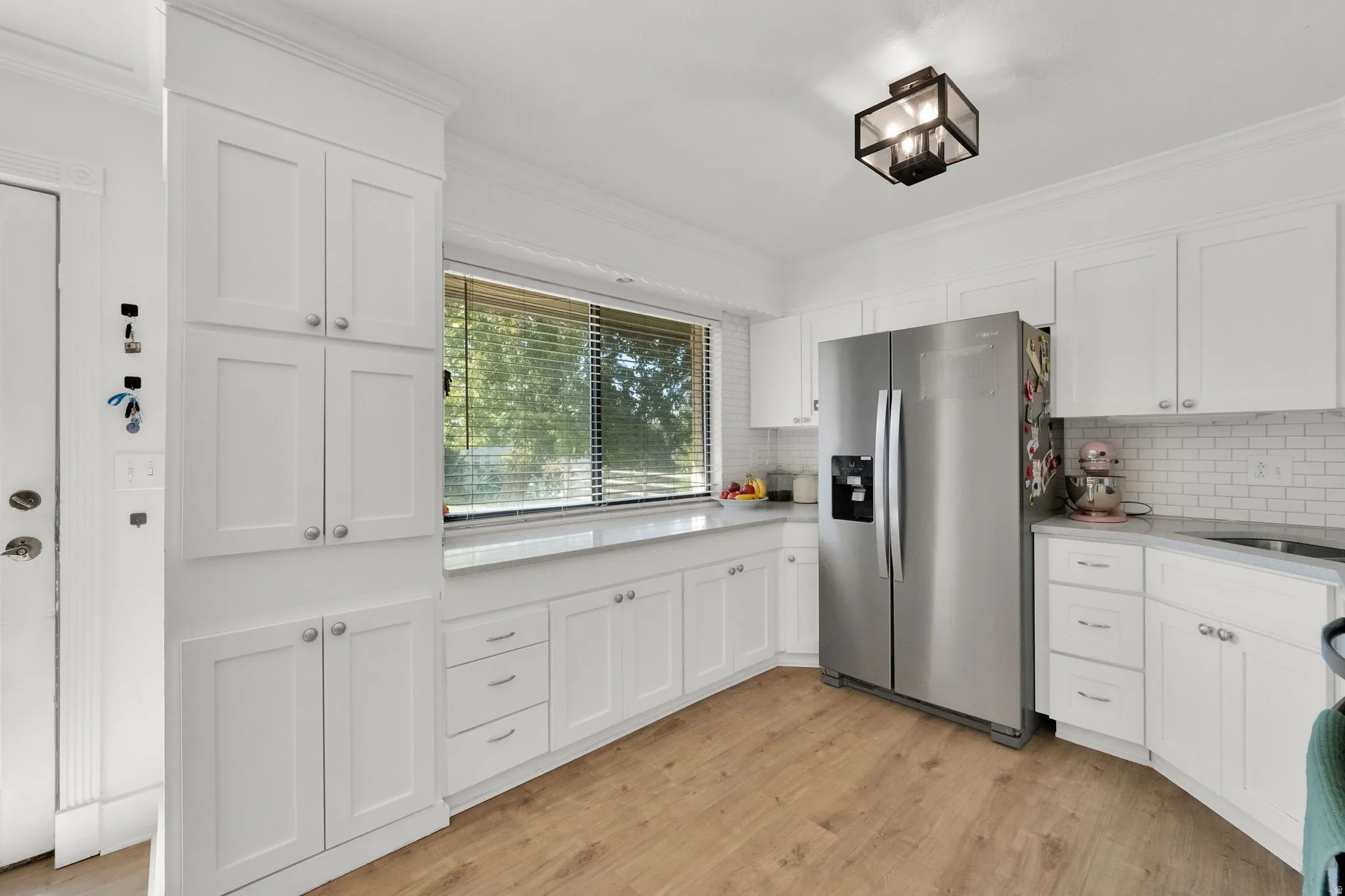 White shaker-style cabinetry, wood-finish flooring, subway tile backsplash, recessed sink basin, and a contemporary ceiling fixture