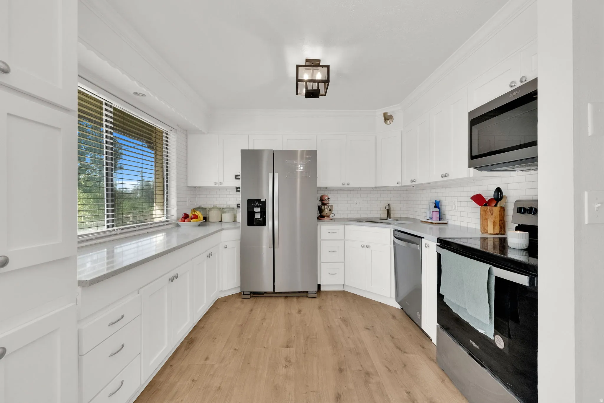 White cabinetry, stainless steel appliances, wood-finish flooring, white subway tile backsplash, and light-toned countertops