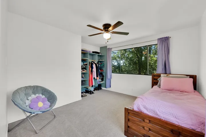Wall-to-wall carpeting, ceiling fan with integrated lighting, built-in shelving, and large window