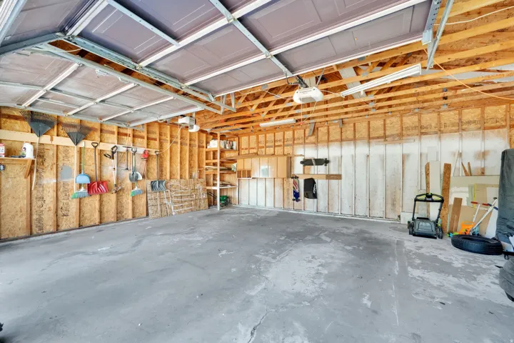 Attached garage with exposed wood framing, concrete flooring, overhead lighting, and built-in shelving