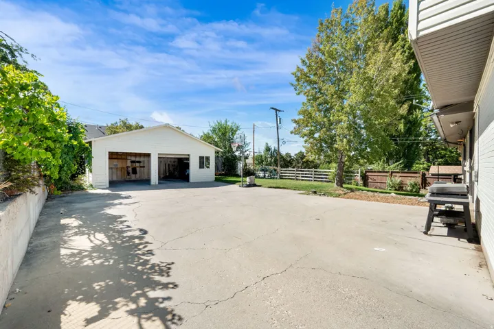 Detached two-car garage with white siding, expansive paved surface, and mature trees
