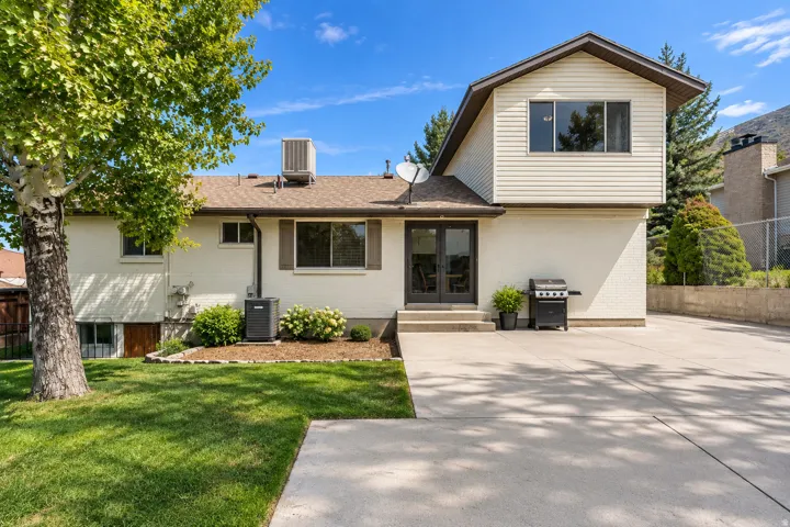 Exterior featuring a white brick and beige siding facade, multiple windows, double glass doors, and a concrete patio