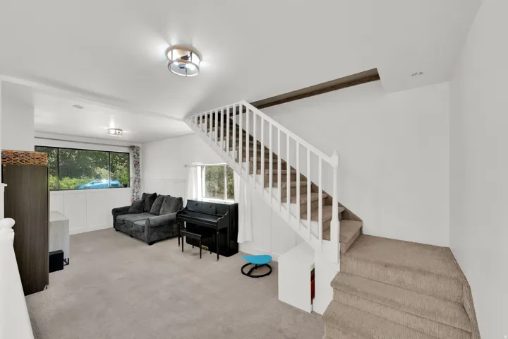 Carpeted living space with a multi-pane window, flush-mount ceiling lighting, and a carpeted staircase with white balusters