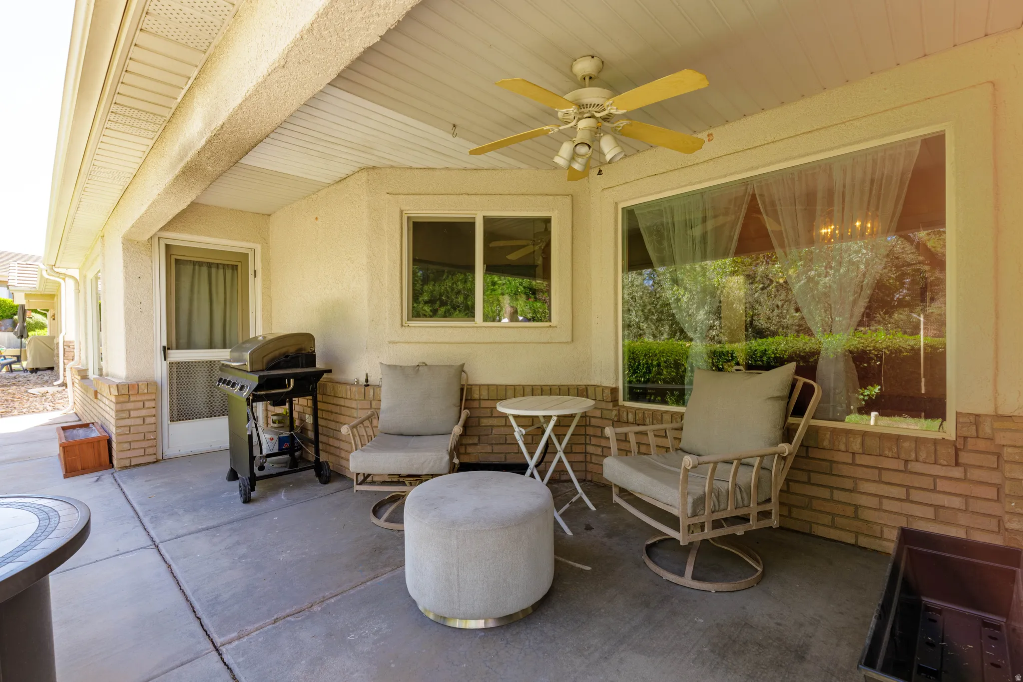 Covered patio with concrete flooring, stucco exterior, brick accents, and a ceiling fan with integrated lighting