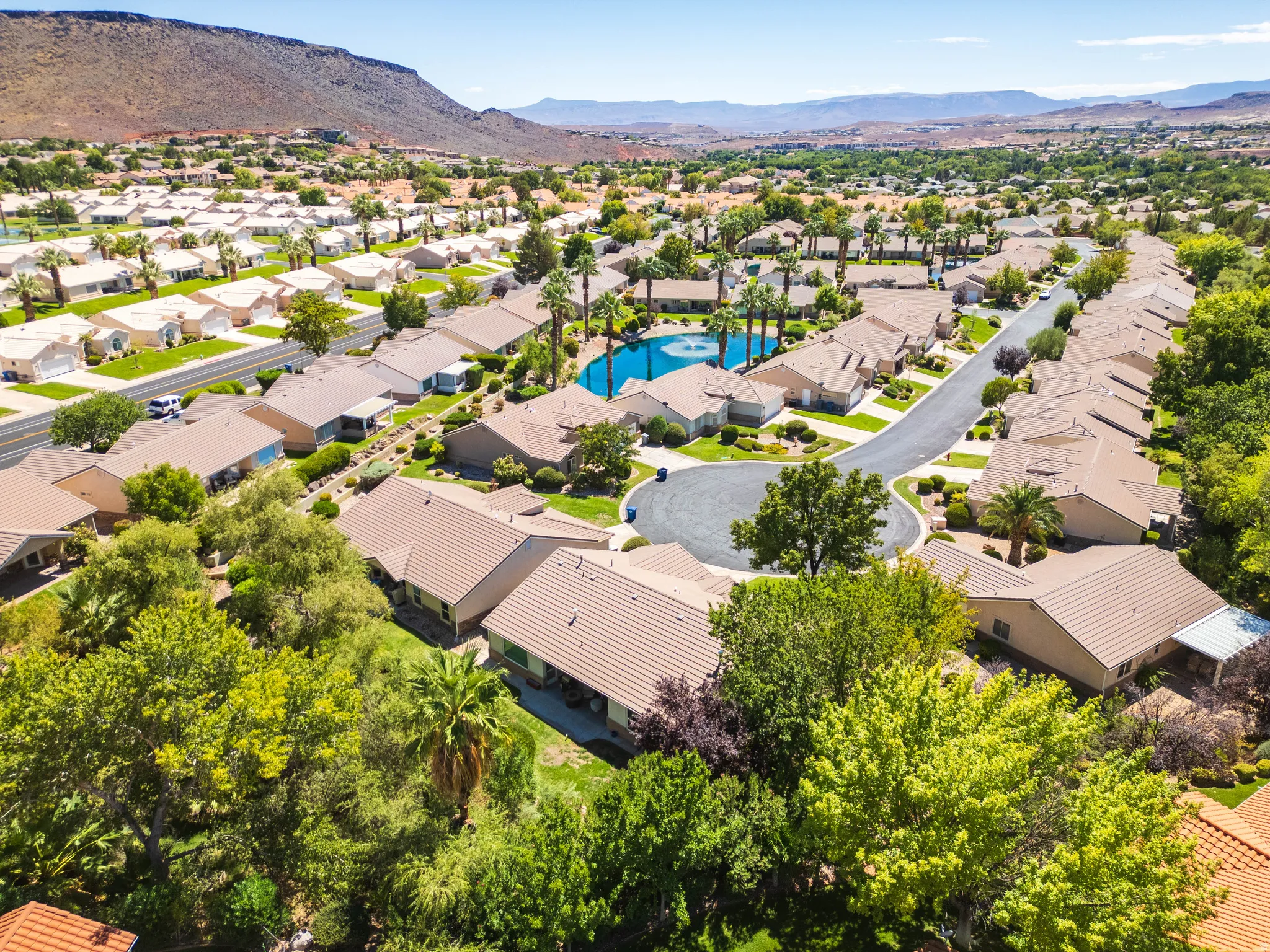 Residential neighborhood with mature trees, a central pond feature, and distant mountainous terrain