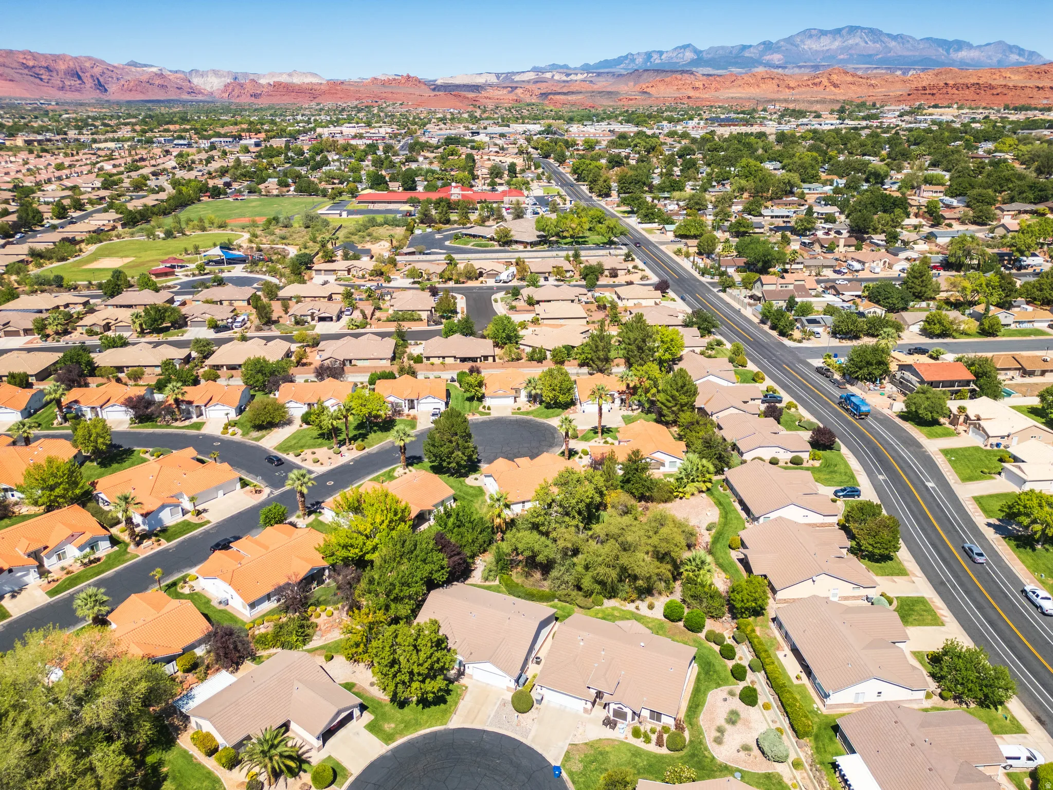 Residential neighborhood with single-story homes, mature landscaping, paved streets, and distant red rock formations